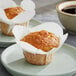 Two Baker's Mark white paper-wrapped muffins on white plates.