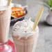 A glass of milkshake with whipped cream and sprinkles with two HAY! wheat straws.