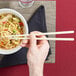 A person holding Town 10 1/2" ivory plastic chopsticks to a bowl of noodles.