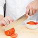 A person using a Dexter-Russell V-Lo Santoku chef knife to cut tomatoes.