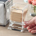 A hand holding a Choice Acrylic Toothpick Dispenser box on a hotel buffet counter.