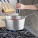 A silver Vollrath Wear-Ever sauce pan with red liquid being poured into it on a stove.