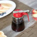 A Tablecraft glass syrup dispenser with a red lid.
