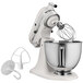 A white KitchenAid stand mixer with a whisk attachment.