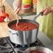 A person cooking red sauce in a Vollrath Wear-Ever sauce pan.