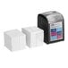 A black Tork Xpressnap Fit tabletop napkin dispenser starter kit with a blue label next to a stack of white interfold napkins.