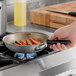 A hand uses a Vollrath Wear-Ever aluminum non-stick fry pan with a black handle to cook carrots on a stove.