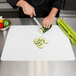 A person cutting a cucumber on a Tablecraft white flexible cutting board.