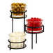 A Cal-Mil black 3-tier condiment display with three glass jars filled with green olives, red berries, and white round objects.