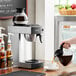 A person pouring coffee into an Avantco commercial coffee maker on a counter.