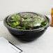 A black Fineline PET plastic bowl filled with salad with a clear lid.