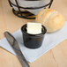 A black Tuxton ramekin filled with butter next to a roll