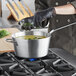 A person in gloves pouring soup into a Vollrath Wear-Ever sauce pan on a stove.