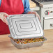 A woman holding a Western Plastics foil steam table pan lid over a tray of food.
