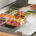 A person in gloves using a Choice clear polycarbonate food pan to fill a container with food at a salad bar.