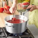 A person cooking red sauce in a Vollrath Wear-Ever sauce pan.