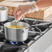 A person using a Vollrath Wear-Ever sauce pan to cook soup on a stove.