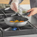 A person cooking food in a Vollrath Wear-Ever non-stick fry pan on a gas stove.