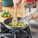 A person cooking food in a Vollrath Wear-Ever aluminum non-stick fry pan with a wooden spatula.