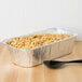 A tray of macaroni and cheese in a Western Plastics foil pan next to a spoon.