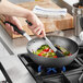 A person cooking food in a Vollrath carbon steel stir fry pan.