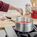 A person in gloves cooking red sauce in a Vollrath Wear-Ever aluminum sauce pan.
