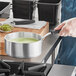 A person holding a Vollrath Wear-Ever sauce pan filled with green liquid on a stove.