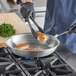 A person cooking food in a Vollrath Wear-Ever aluminum fry pan with a black silicone handle.