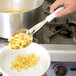 A person using a Vollrath Jacob's Pride perforated basting spoon with a white handle to serve pasta.