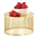 A round gold metal display riser with a round white object and raspberries on top.
