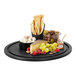 A Cal-Mil round black wood serving board with cheese, grapes, and crackers on it.