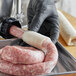 A person in a black glove using a white rope to wrap sausages on a tray.