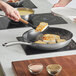 A person using a Vigor SS3 Series stainless steel non-stick fry pan to cook food.