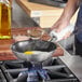 A Vigor SS3 Series stainless steel frying pan with a fried egg in it being cooked on a stove.
