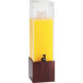 A dark wood Cal-Mil beverage dispenser with a glass container of yellow liquid.