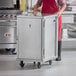 A woman in a red apron standing next to a Regency stainless steel enclosed sheet pan rack.
