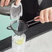 A person using a Barfly vintage black conical fine mesh strainer to pour a drink.