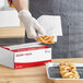 A person wearing gloves putting pastries into a box using Choice interfolded bakery tissue.