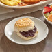 A Bakery Chef buttermilk biscuit with jam on a plate next to a bowl of fruit.