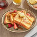 A plate of Krusteaz Cinnamon Swirl French Toast with butter and strawberries on top.