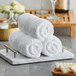 A stack of three white Lavex Luxury hand towels on a tray.