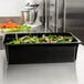 A black Cambro food pan filled with green and red lettuce leaves on a kitchen counter.