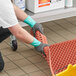 A person wearing green Ansell AlphaTec dishwashing gloves cleaning a plastic mat.