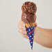 A hand holding a chocolate ice cream cone with a scoop of Eclipse Foods Vegan Chocolate Ice Cream.