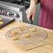 A person putting cookies on a Choice round cooling rack.