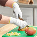 An Ansell HyFlex cut-resistant glove cutting a mango on a cutting board.