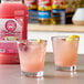 Two glasses of Lotus Plant Energy Skinny Pink Lemonade with a bottle of pink lemonade.