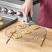 A person using a spatula to place a cookie on a Choice round footed cooling rack.