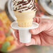 A hand holding a small ice cream cone in a plastic cone holder on a counter.