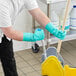 A man wearing green Ansell AlphaTec Solvex gloves cleaning a floor with a mop.
